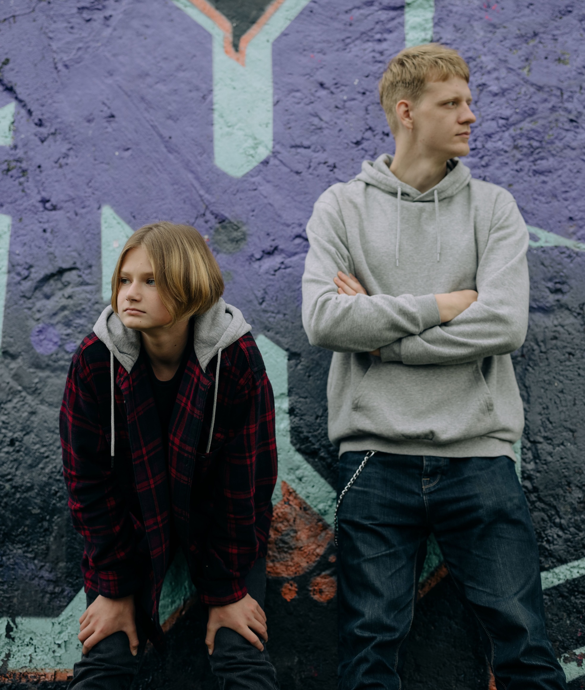 Two teenagers stand against a vibrant graffiti wall, embracing urban youth style.